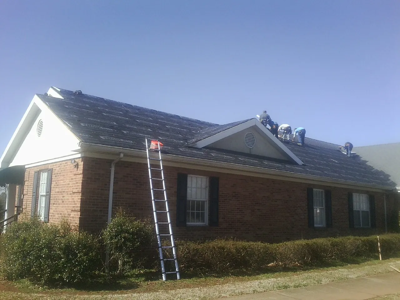 Crew tearing shingles off a brick ranch roof with a ladder set — Emergency Roof Repair work by our crew in Horsham