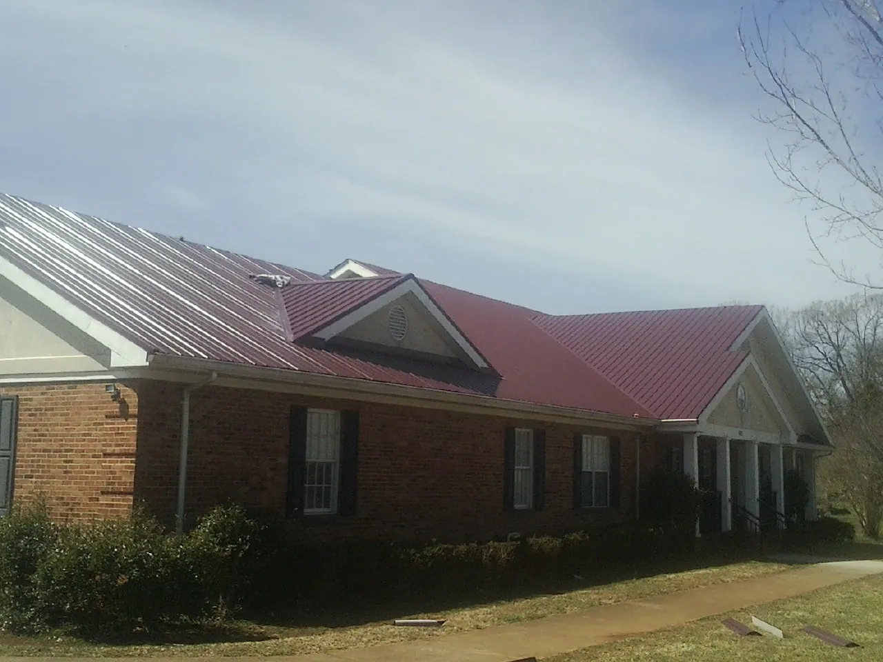 Red metal roof with gabled entries on a long brick building, from a Hail Damage Roof Repair job in Horsham
