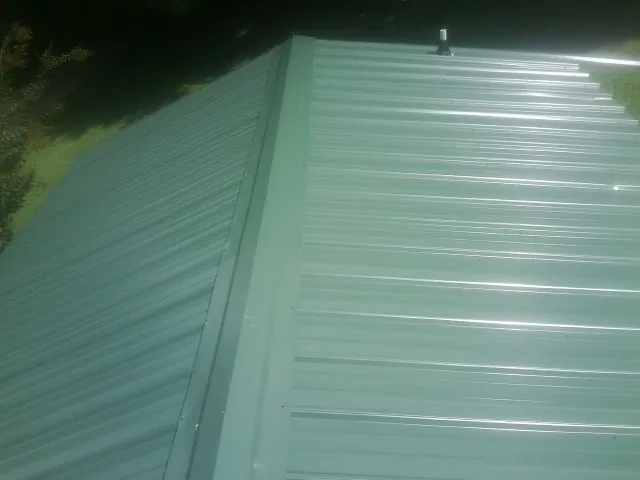 New green metal panels meeting at the ridge of a roof — Flat Roof Repair work by our crew in Horsham