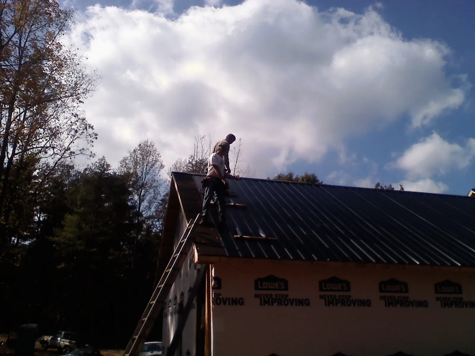 Roofer fastening dark metal panels high against a cloudy sky, from a Roof Inspection job in Horsham