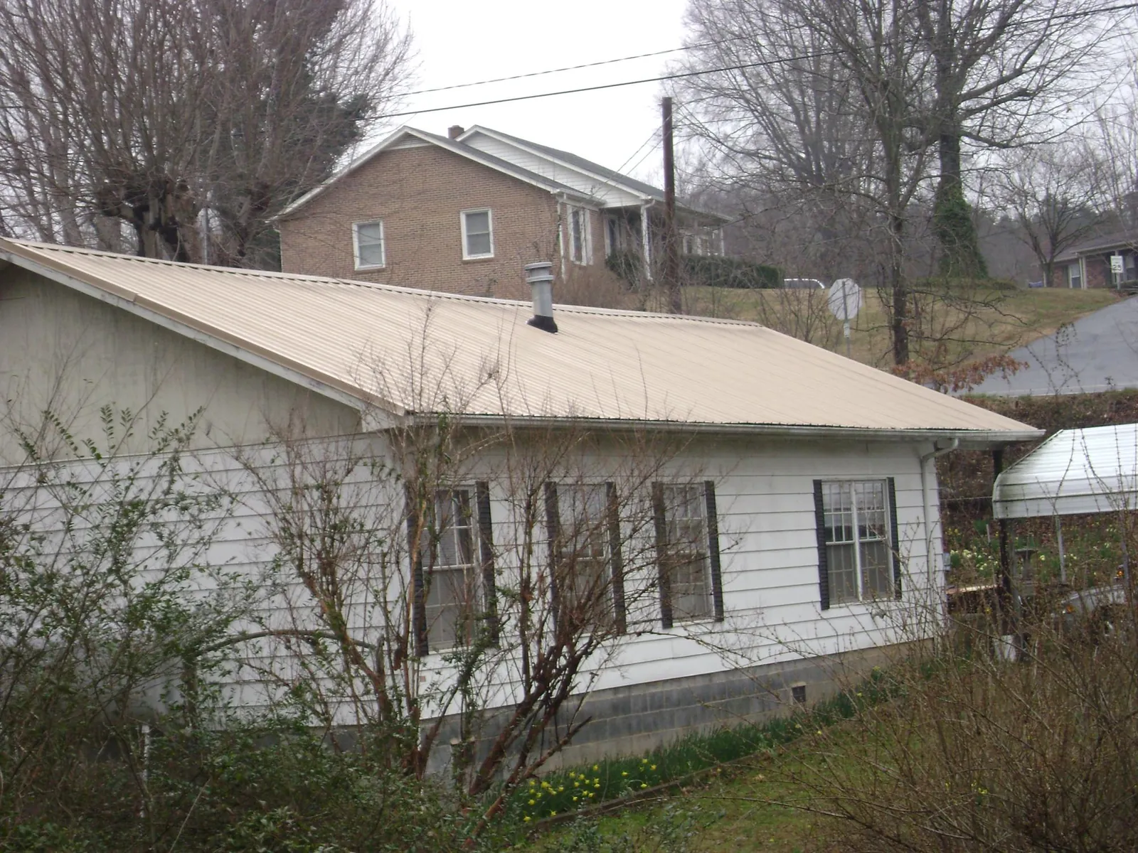 Tan metal roof on a white sided house set into a hillside — Commercial Roofing by Roofing Brothers in Horsham